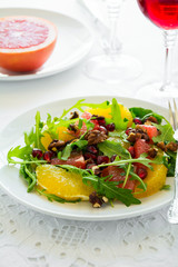 Fresh salad with arugula, orange, grapefruit, walnuts and pomegranate seeds on white table cloth. Healthy food.