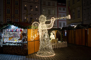 Christmas market on the square, Prague, Czech Republic / Czechia. Angel made of lights and bulbs, Exterior shop in the wooden booth and stand. Event during Advent and xmas holiday