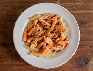 Cooked Penne Pasta Dish, with vibrant red tomato sauce on top, and sprinkled oregano, on a white porcelain plate, dark wood background tabletop