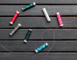 Colorful and colored sewing threads spread over a dark wooden background, closeup, with copy space
