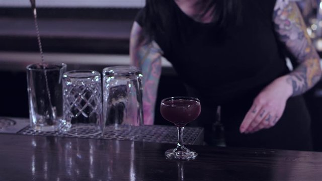 Tattooed bartender lady puts a cherry into an alcoholic drink, and then pushes the drink towards the camera 
