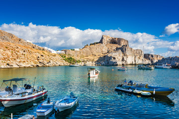 Fishing boats, zodiac boat, jet ski in St. Paul´s bay, Lindos acropolis in background (Rhodes, Greece)