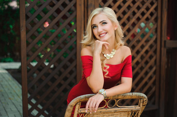 Fashionable attractive blonde woman in red dress sitting on chair.