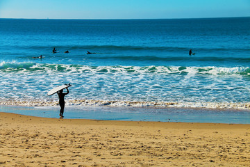 A man carrying his board to surf with other surfers on the beach of El Palmar, on the coasts of...