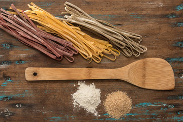 Three coloured dry pasta over wooden top with wooden spoon
