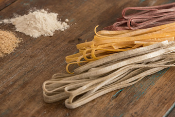 Three coloured dry pasta over wooden top with wooden spoon