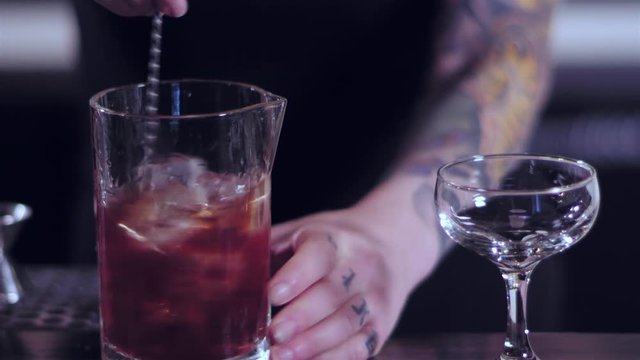 Close up shot of a bartender stirring an alcoholic drink, and then pouring it onto a drinking glass at a bar