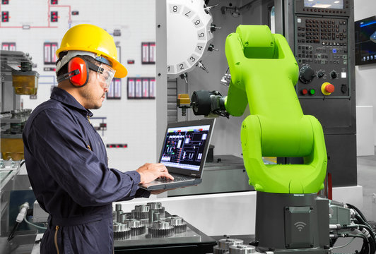 Engineer using laptop computer control automatic robotic hand machine tool with CNC machine in automotive industry, Industry 4.0 concept