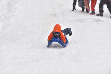 Fototapeta na wymiar Little boy riding on snow slides in winter time