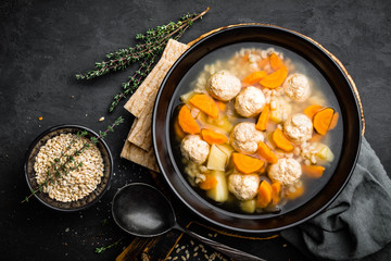 Fresh vegetable soup with meatballs and pearl barley in bowl on black background. Top view
