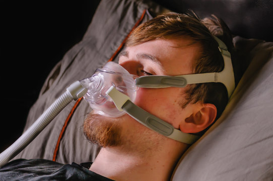 A young man in bed at night using a CPAP machine with face mask