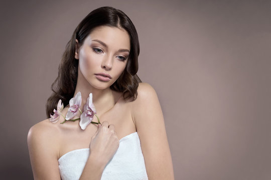 Young and healthy woman with light make-up is holding the Orchid flower. Beige background.