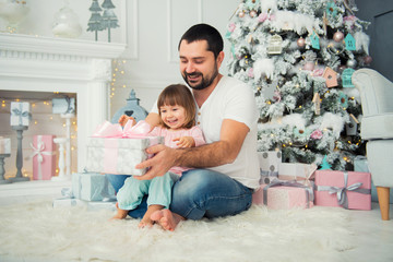 Big father and happy little daughter open New Year's gifts near the Christmas tree