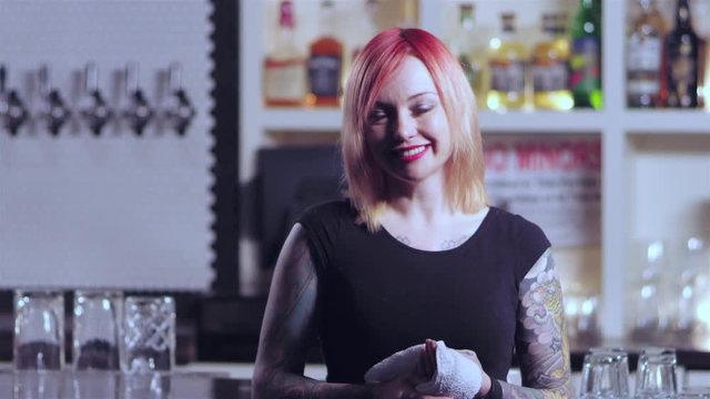 Portait shot of an attractive tatttoed bartender lady showing different emotions, while holding a towel at a bar