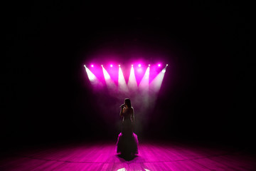 Girl in long gown performing on stage. Girl singing on the stage in front of the lights. Silhouette...
