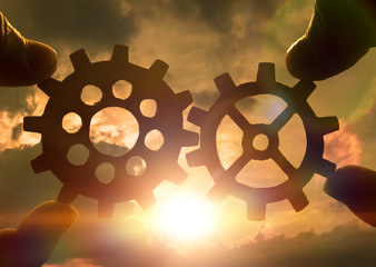 Two hands holding gears together. against the sunset. Close-up. Teamwork, partnership, business, cooperation and management concept.