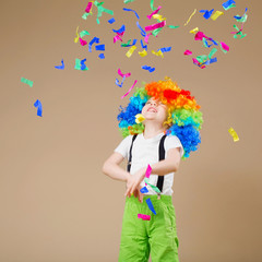 Happy clown boy with large colorful wig. Let's party! Funny kid clown. 1 April Fool's day concept. Portrait of a child throws up a multi-colored tinsel and confetti.