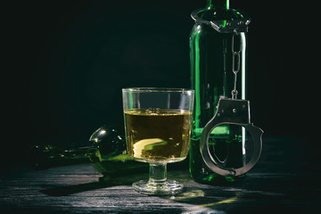 Bottles and glass of alcohol on wooden table against black background. Concept of bad habits