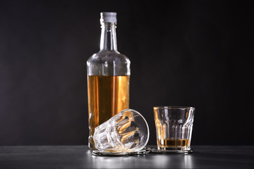 Bottle and glasses with handcuffs on dark background. Alcohol dependence concept
