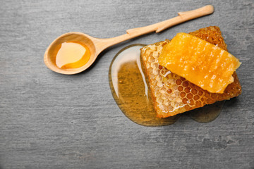 Fresh honeycombs and wooden spoon with honey on grey background