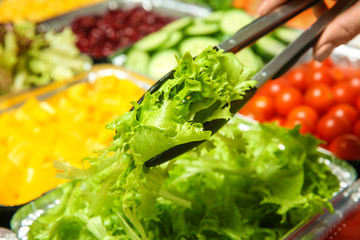 Woman taking ingredient for salad, close up