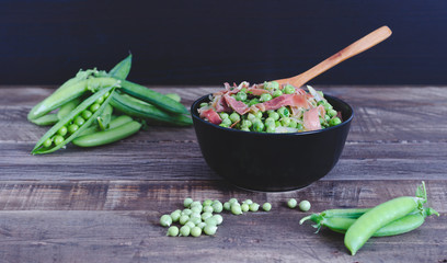 Bowl with peas and ham on wooden background.