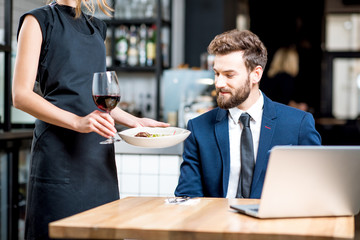 Handsome businessman with young waitress carriyng a meal on the background sitting at the restaurant during a dinner