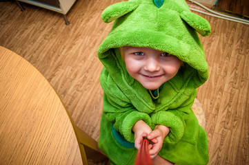 Funny little boy in a green robe with a hood looks from below
