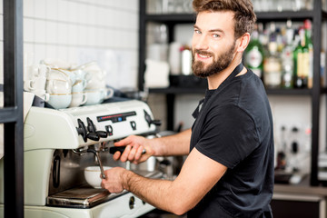 Handsome barista making coffee with coffee machine at the bar of the modern cafe