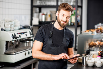 Handsome waiter in black t-shirt working with tablet standing at the bar of the modern cafe interior
