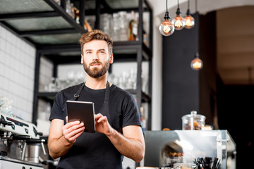 Handsome waiter in black t-shirt working with tablet standing at the bar of the modern cafe interior