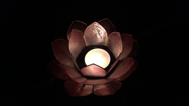 Candle burning in lotus flower with black and empty background.
