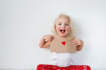 Portrait of adorable small kid has cheerful expression, holds letter to Santa Claus, hopes her...