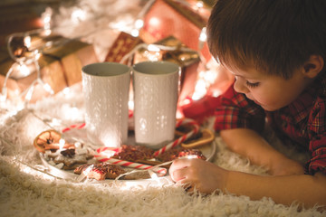 Boy laying under christmas tree with chocolate drink.