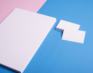 Business cards and stacked sheets of paper in white on pink and blue background. Mockup.