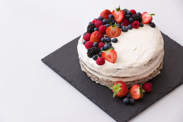 Delicious homemade nake cake decorated with fresh organic berries: blueberry, strawberry and raspberry on black board.