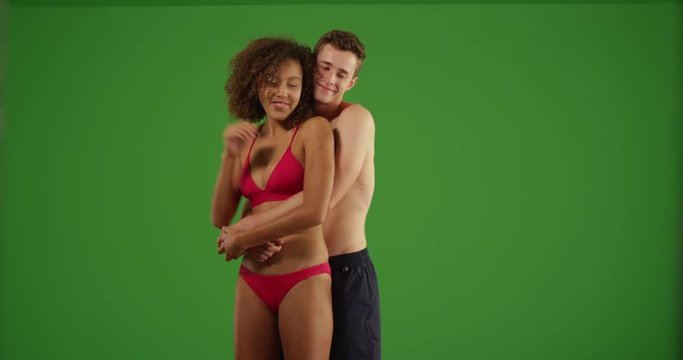 Young happy millennial couple dancing on tropical beach holding each other and looking into the distance on green screen. On green screen to be keyed or composited. 