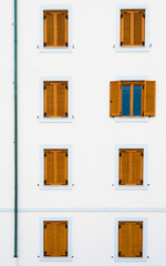 White building with closed windows, one window is opend, brown shutters.