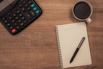 Calculator and cup of coffee with note on working table with copy space top view.