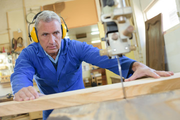senior male carpenter using table saw for cutting wood
