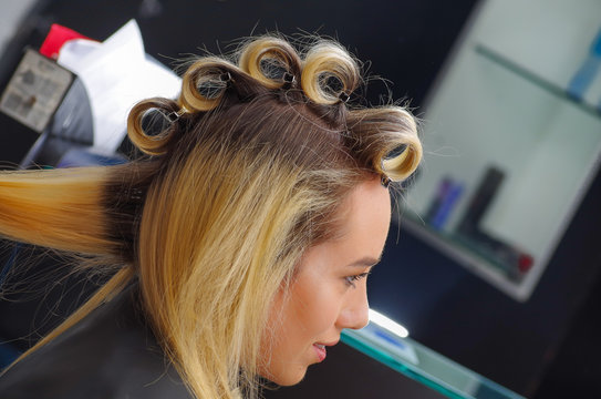 Portrait of beautiful woman in a hair salon with a stylist working with curlers in the head, in a hair salon background