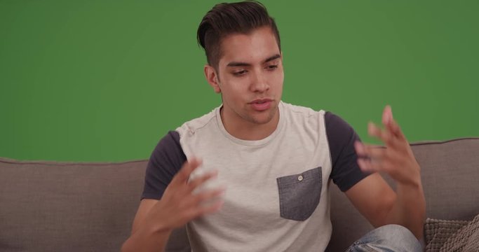 Young millennial Hispanic man talking to camera on green screen. On green screen to be keyed or composited. 