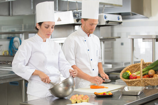 chef teaching colleague how to slice vegetables in the kitchen