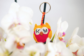 Small pink and yellow handmade knitted owl hanging indoors on a branch of a white Orchid plant