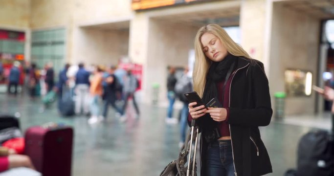 Traveling blonde white female checks smartphone at busy airport 