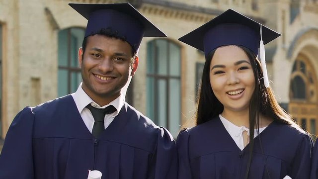 Multiracial exchange students celebrating graduation, posing with diplomas