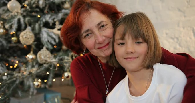 Little girl hugging her grandmother. Family exchanging gifts at Christmas. They looking at camera. Christmas holiday and New Year.