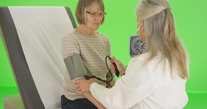 A elderly patient gets her blood pressure checked by her doctor on green screen. On green screen to be keyed or composited. 