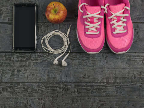 Beautiful pink sneakers, headphones, water and apples on a wooden black floor. View from above.