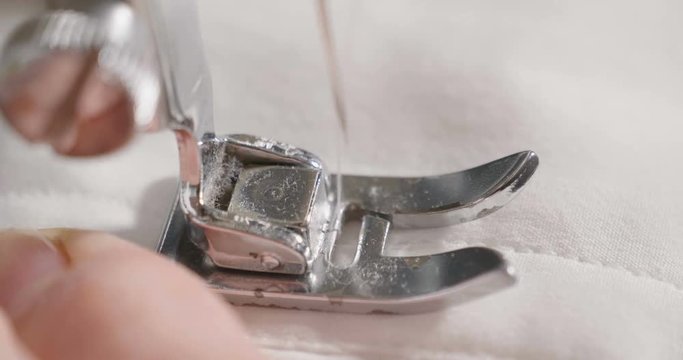 Super slow motion of middle-age woman hand stitching on white fabric with vintage sewing machine (macro close up)